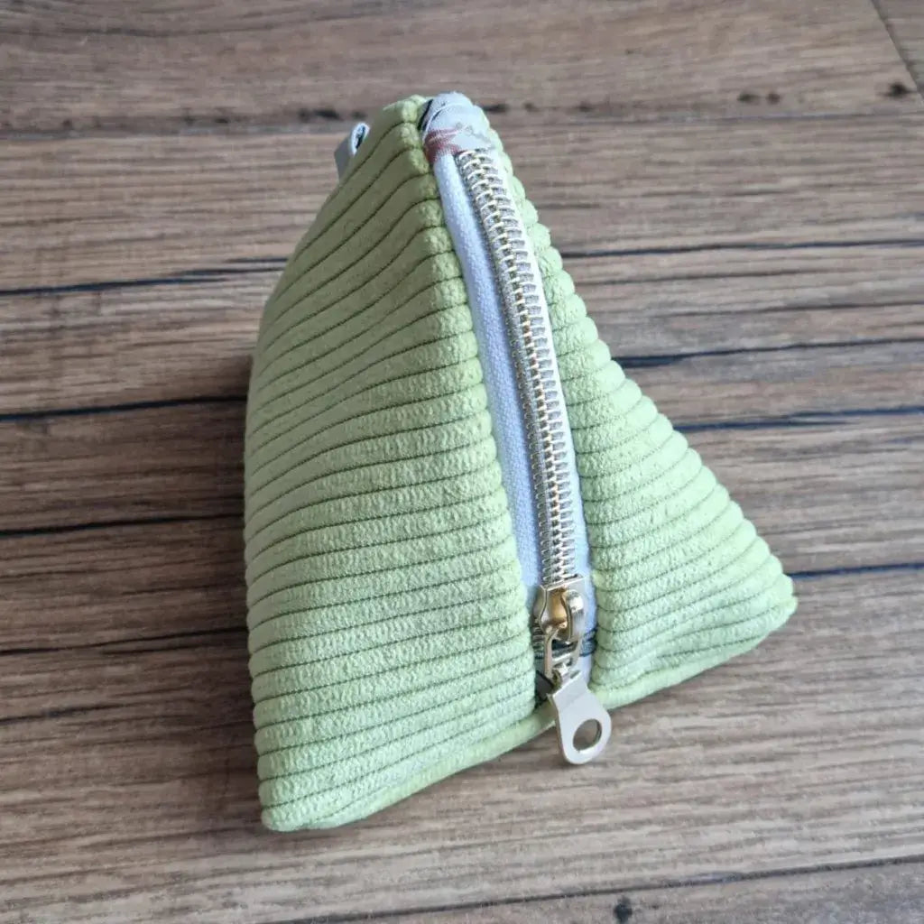 Trousse berlingot triangulaire vert anis en velours côtelé, zip doré et tirette anneau posée sur bois