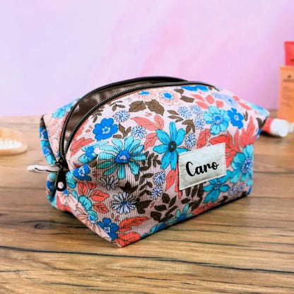 Trousse carrée personnalisée en tissu à motif fleuri vintage, décorée de fleurs turquoise, corail et marron sur fond clair. Fermeture éclair dorée et étiquette en tissu floquée du prénom “Caro”. Accessoire de rangement fait main idéal pour le maquillage, les soins ou les voyages. Design coloré et féminin, parfait comme cadeau personnalisé artisanal fabriqué en France.