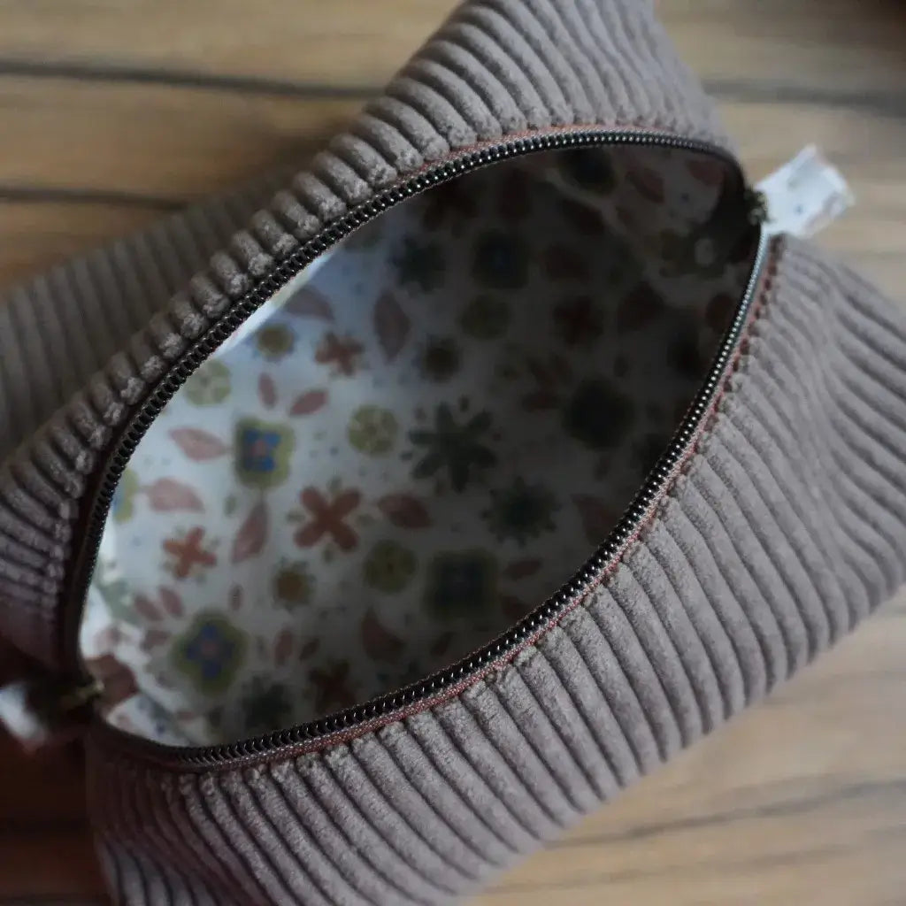Trousse carrée en velours côtelé taupe ouverte, laissant apparaître sa doublure intérieure en coton imprimé de motifs floraux aux teintes douces. Accessoire fait main idéal pour ranger maquillage, stylos ou petits objets du quotidien. Fermeture zippée résistante et finitions soignées, symbole du savoir-faire artisanal et de la couture française personnalisée.