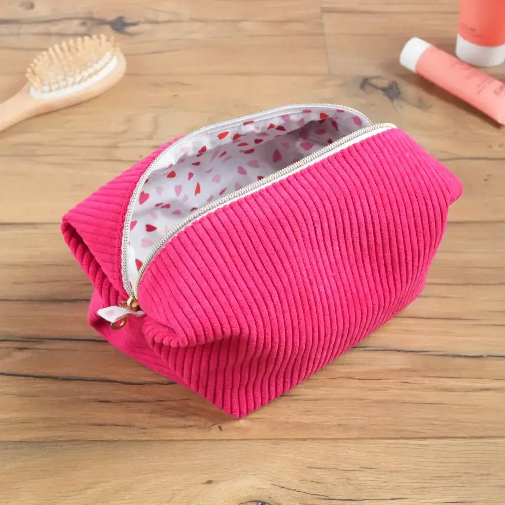 Trousse carrée en velours côtelé framboise ouverte, laissant entrevoir sa doublure blanche parsemée de petits cœurs rouges. Son ouverture large et sa fermeture dorée garantissent un accès facile aux produits de beauté ou accessoires du quotidien. Fait main avec soin, cet accessoire coloré allie douceur, praticité et charme artisanal pour une trousse à la fois utile et décorative.