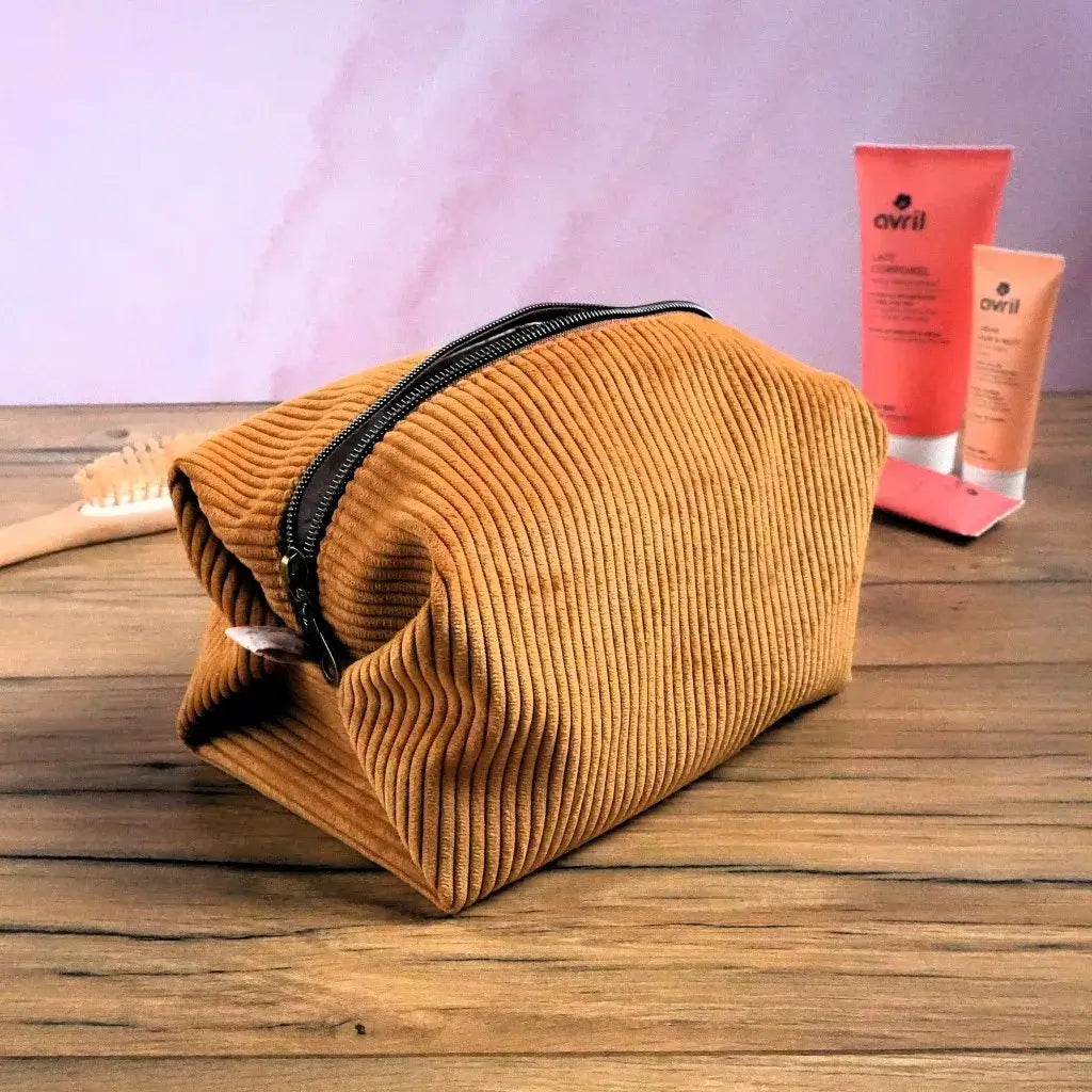 Trousse carrée en velours côtelé couleur jaune posée sur une table en bois, accompagnée de produits de beauté. Sa fermeture éclair marron contrastante souligne son design moderne. Pratique et spacieuse, elle permet de ranger facilement maquillage, soins ou accessoires. Confectionnée à la main, cette trousse personnalisable allie douceur du velours et élégance artisanale.