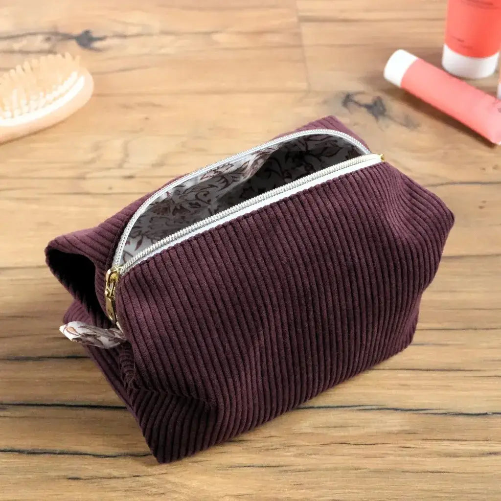 Trousse carrée en velours côtelé prune avec fermeture dorée, dévoilant une élégante doublure en coton imprimé floral. Sa texture douce et son ouverture large facilitent le rangement des accessoires de beauté, maquillage ou essentiels du quotidien. Confectionnée à la main, cette trousse personnalisable allie sobriété, charme et qualité artisanale française.