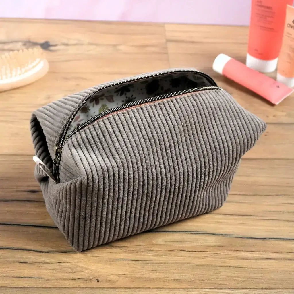 Trousse carrée en velours côtelé taupe, ouverte pour révéler sa doublure en coton à motifs fleuris. Son zip métallique assure une fermeture solide et une ouverture large pour un accès facile. Élégante et fonctionnelle, cette trousse artisanale personnalisable est idéale pour ranger maquillage, accessoires ou produits de soin avec style et praticité.