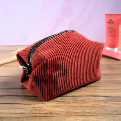 Trousse carrée en velours côtelé terracotta posée sur une table en bois, avec fermeture éclair marron et finitions soignées. Sa texture douce et son format généreux offrent un rangement pratique pour le maquillage, les accessoires ou les produits de soin. Réalisée à la main, cette trousse personnalisable séduit par son style chaleureux et son allure artisanale élégante.