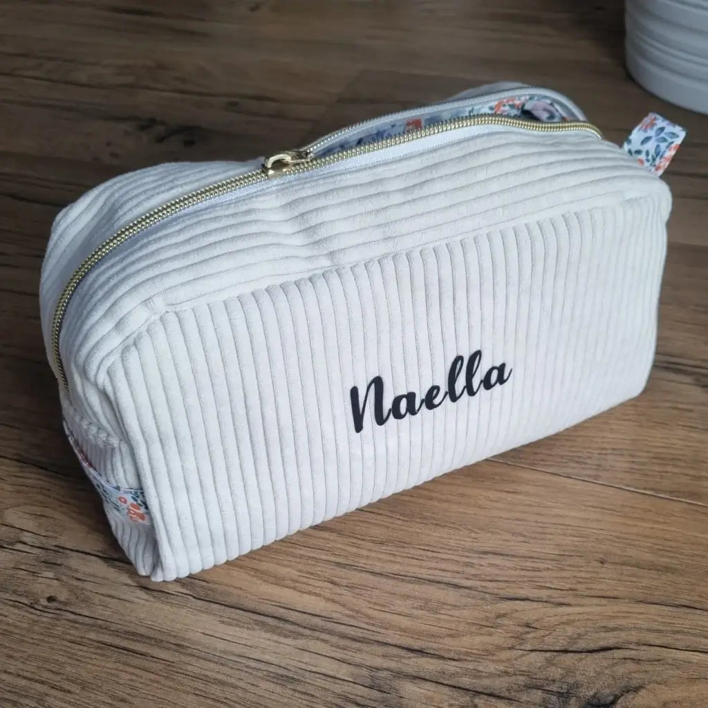 Trousse de toilette en velours côtelé beige avec son zip ouvert laissant apparaître un tissu intérieur imprimé fleuri.