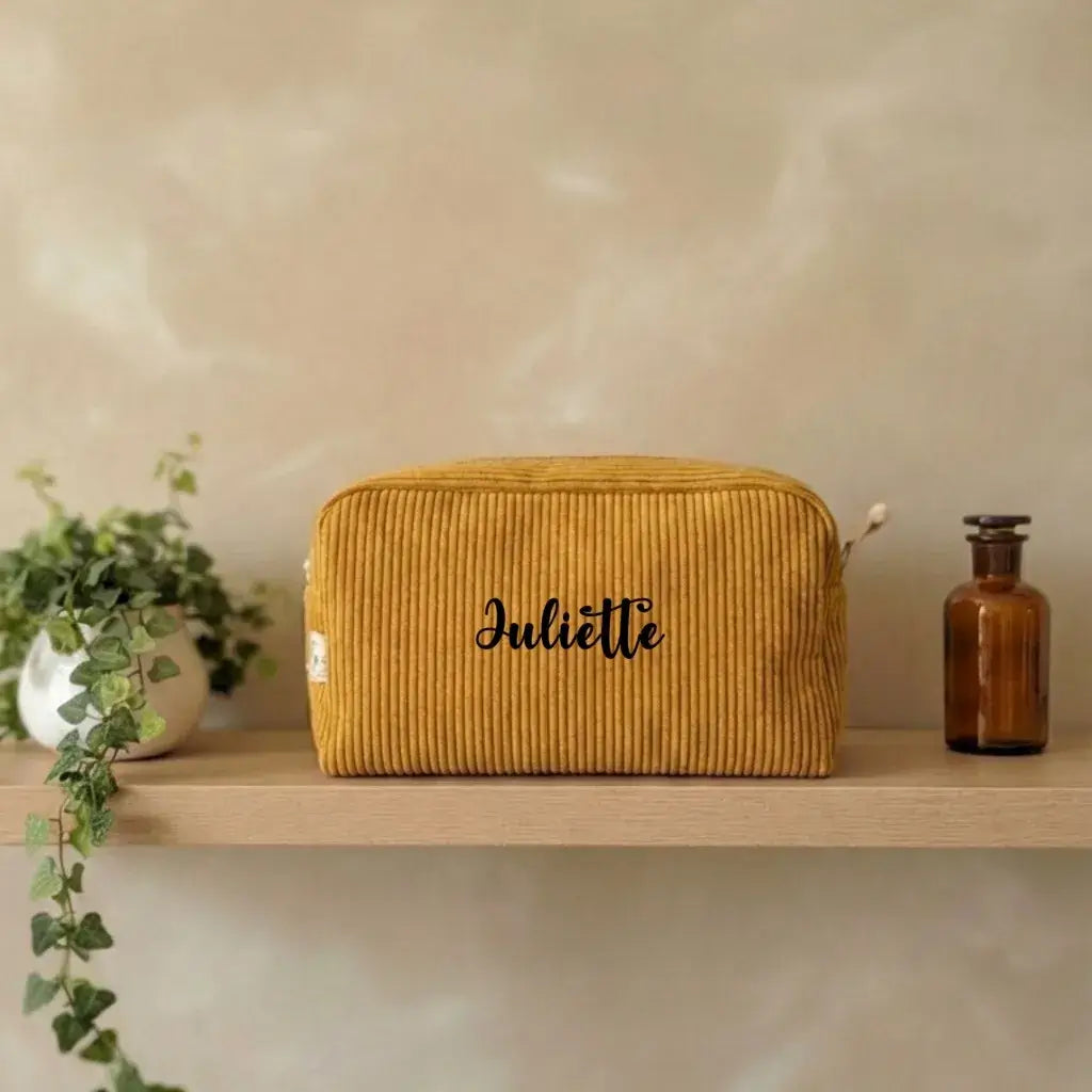 Trousse de toilette velours côtelé jaune moutarde personnalisée Juliette sur une étagère en bois.