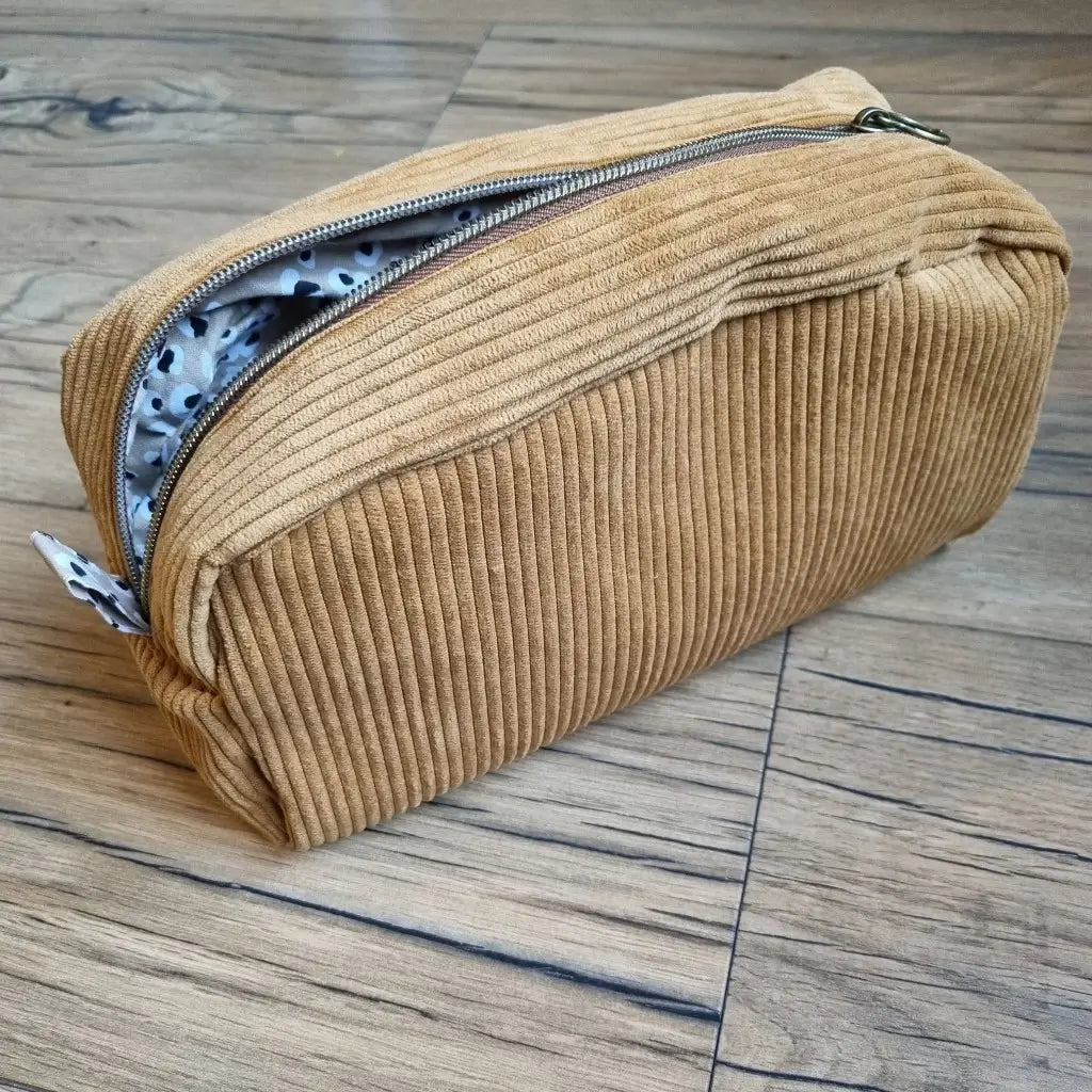 Trousse de toilette en velours côtelé jaune avec son zip ouvert laissant apparaître un tissu intérieur au motif léopard.