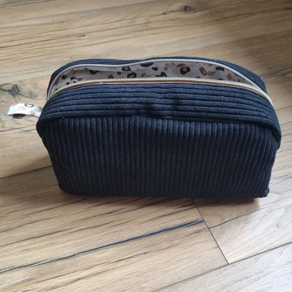 Trousse de toilette en velours côtelé noir avec son zip ouvert laissant apparaître un tissu intérieur imprimé léopard.