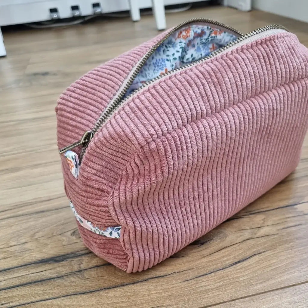 Trousse de toilette en velours côtelé rose avec son zip ouvert laissant apparaître un tissu intérieur au motif fleuri.