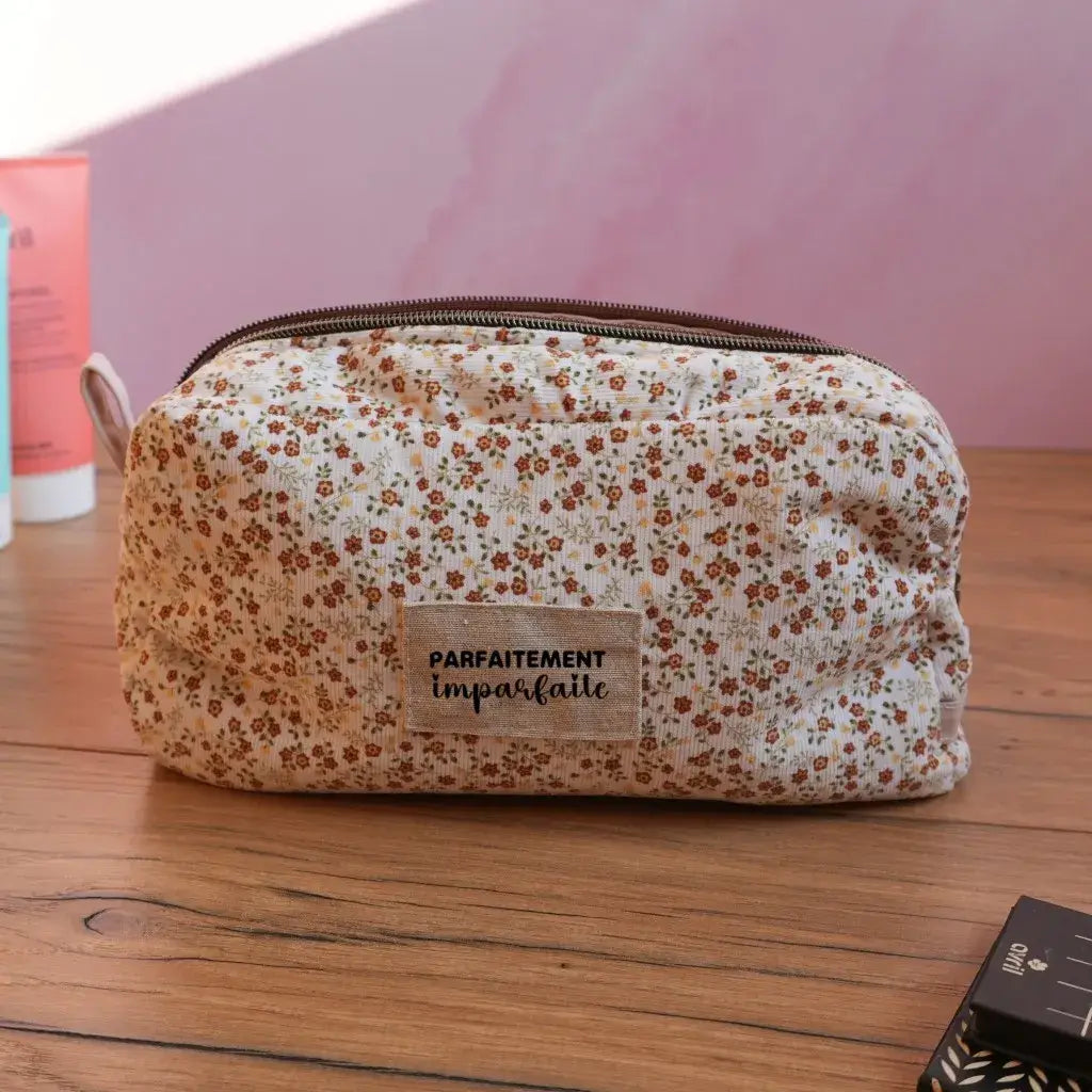 Trousse de toilette en tissu crème décorée de petites fleurs champêtres, avec étiquette « Parfaitement imparfaite ». Élégante et fonctionnelle, cette trousse zippée au style bohème est parfaite pour ranger maquillage, produits de soin et accessoires beauté. Son format pratique et son design fleuri en font un indispensable du quotidien comme des voyages.
