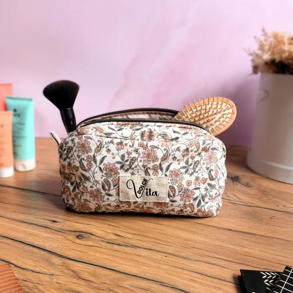 Trousse de toilette en tissu à motifs floraux délicats, ornée d’une étiquette floquée « Dolce Vita », posée sur une table en bois avec pinceau et brosse à cheveux. Idéale comme trousse de maquillage ou pochette de voyage, elle allie praticité et élégance pour organiser vos essentiels beauté avec style. Son format compact et esthétique en fait un allié incontournable.