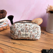 Trousse de toilette en tissu fleuri beige et rose, ornée d’une étiquette en tissu floquée « Parfaitement imparfaite », remplie d’accessoires beauté comme un pinceau et une brosse. Pratique et élégante, cette trousse zippée est parfaite pour organiser maquillage, soins et accessoires de voyage. Son design artisanal et tendance en fait un indispensable beauté au quotidien comme en déplacement.