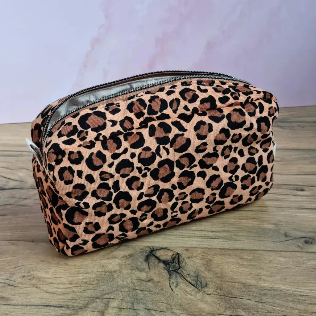 Grande trousse de toilette rectangulaire en velours léopard avec zip, posée sur un plan de travail en bois.