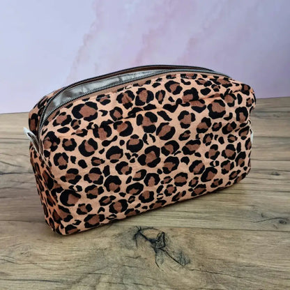Grande trousse de toilette rectangulaire en velours léopard avec zip, posée sur un plan de travail en bois.