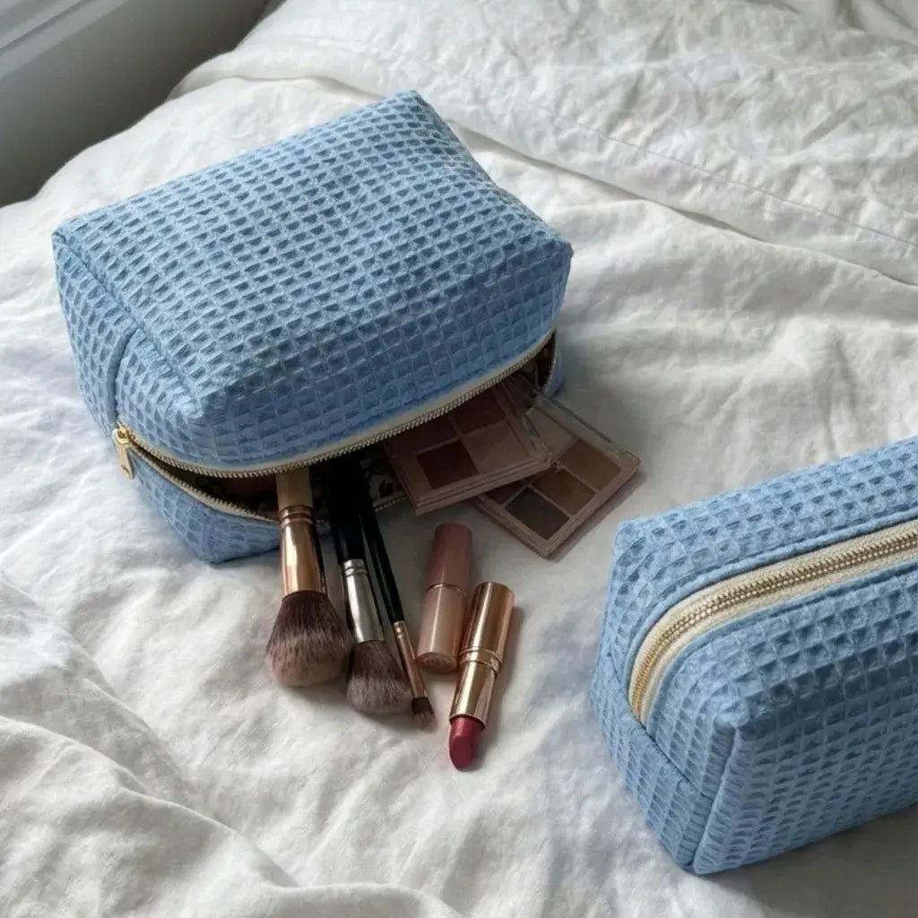 trousse maquillage bleue nid d’abeille avec fermeture éclair et accessoires beauté sur lit