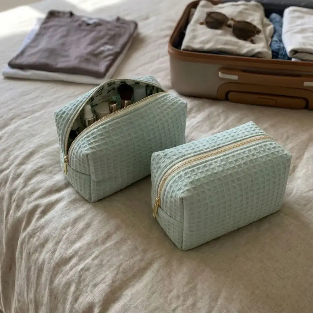 trousse maquillage vert menthe nid d’abeille avec zip posée sur lit près valise ouverte