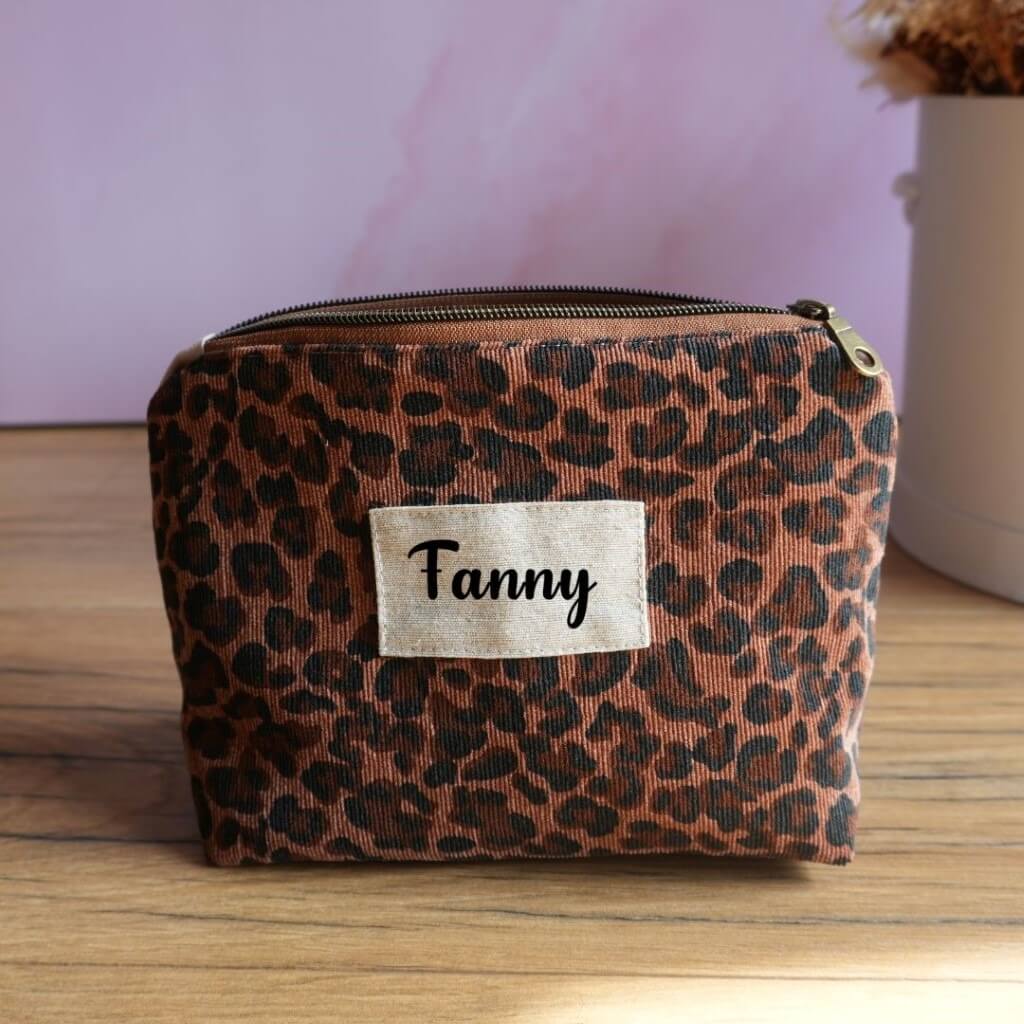 Trousse zippée personnalisée à motif léopard marron et noir, agrémentée d’une étiquette en tissu avec le prénom Fanny floqué en noir. Pochette artisanale tendance et pratique pour ranger maquillage, accessoires de beauté, stylos ou effets personnels. Son design animalier apporte une touche sauvage et moderne, idéale comme cadeau personnalisé ou accessoire du quotidien.