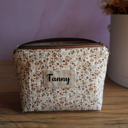 Trousse zippée personnalisée en tissu crème décoré de petites fleurs esprit prairie dans des tons orangés et verts, avec étiquette en lin affichant le prénom Fanny en noir. Pochette artisanale pratique pour maquillage, accessoires ou fournitures, elle associe charme rétro et utilité. Un accessoire élégant et personnalisé, parfait comme trousse de toilette, pochette de sac ou cadeau sur mesure.
