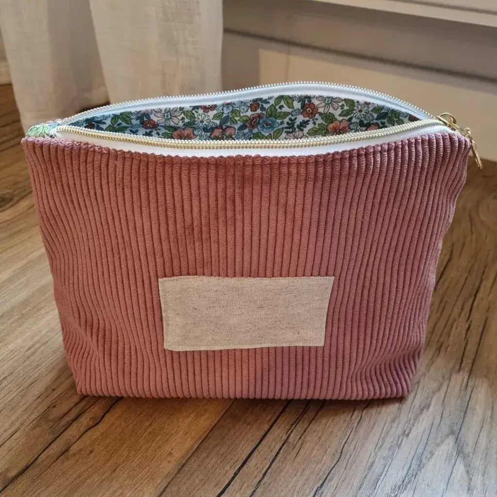 Trousse zippée en velours côtelé rose avec une doublure intérieure en coton imprimé à motif fleuri. Cette trousse dispose d'une étiquette en tissu cousue en façade pouvant accueillir un prénom ou une inscription personnalisée qui sera floquée dessus.