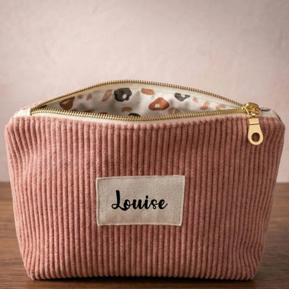 Trousse zippée en velours côtelé rose avec une doublure intérieure en coton imprimé à motif fleuri. Cette trousse dispose d'une étiquette en tissu cousue en façade pouvant accueillir un prénom ou une inscription personnalisée qui sera floquée dessus.