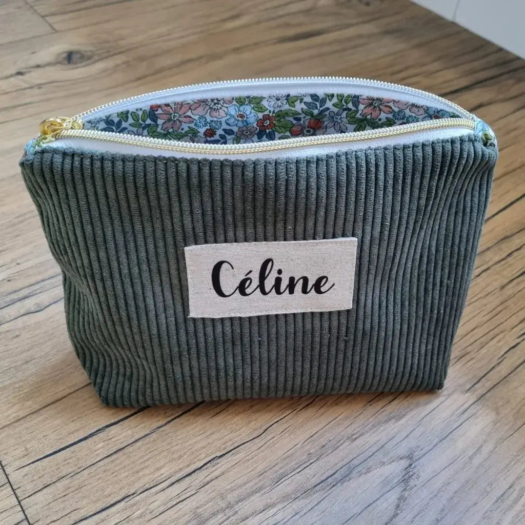 Trousse zippée en velours côtelé vert doublée avec un tissu en coton imprimé à motif fleuri. Cette trousse dispose d'une étiquette en tissu cousue en façade sur laquelle est floqué le prénom "Céline" en écriture noire.