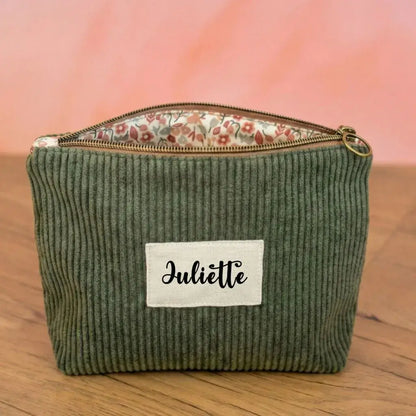 Trousse zippée en velours côtelé vert doublée avec un tissu en coton imprimé à motif fleuri. Cette trousse dispose d'une étiquette en tissu cousue en façade sur laquelle est floqué le prénom "Céline" en écriture noire.