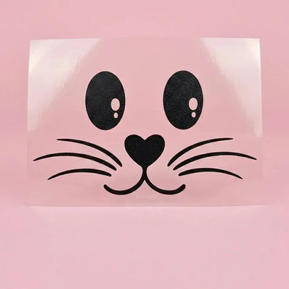 Flex thermocollant noir : visage de lapin avec yeux ovales, nez en cœur et moustaches, sur support transparent et fond rose.