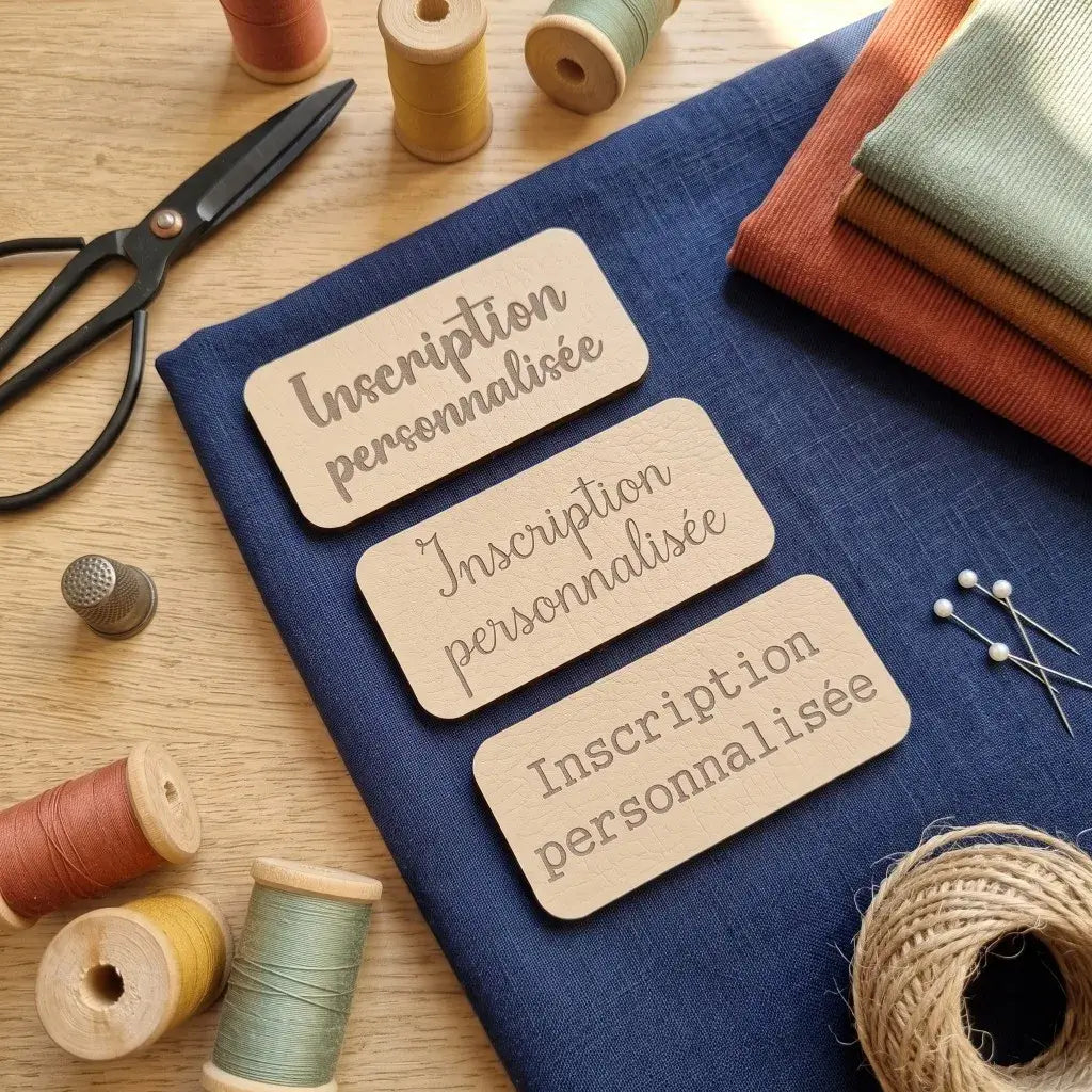 Trois étiquettes à coudre en simili cuir beige gravées Inscription personnalisée, sur tissu bleu avec ciseaux et bobines