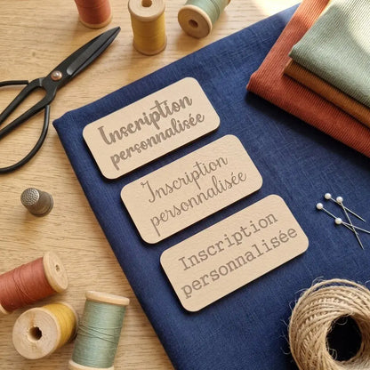 Trois étiquettes à coudre en simili cuir beige gravées Inscription personnalisée, sur tissu bleu avec ciseaux et bobines