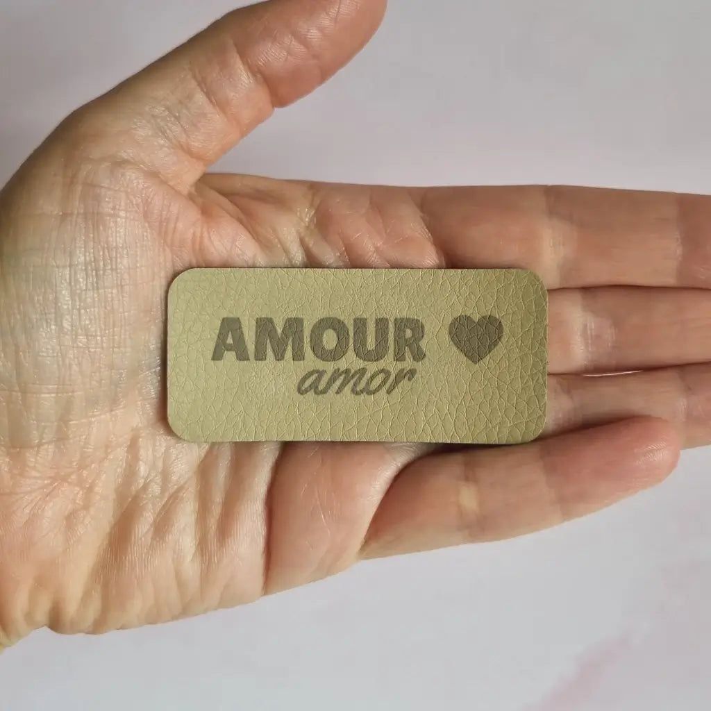 Étiquette à coudre en simili cuir gravée Amour amor avec petit cœur, tenue dans la main