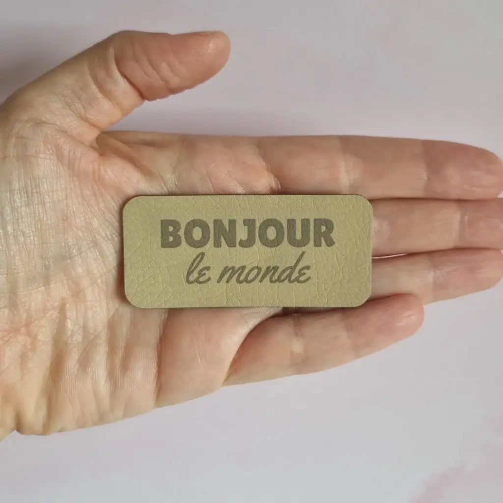Étiquette rectangulaire en simili cuir gravée Bonjour le monde, tenue à la main
