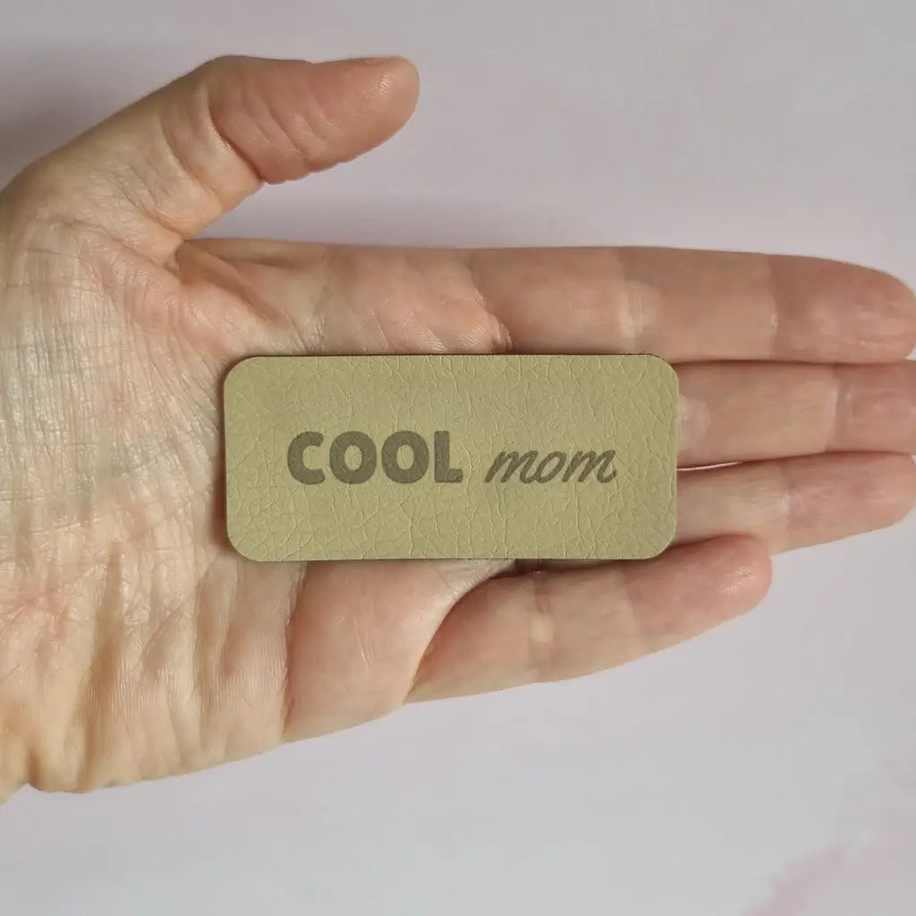 Étiquette à coudre en simili cuir gravée Cool mom, sans motif, posée dans la main