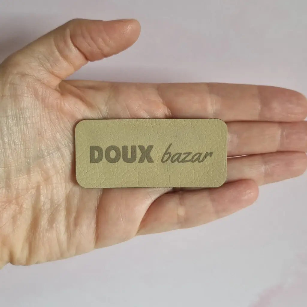Étiquette à coudre en simili cuir gravée Doux bazar, tenue au creux de la main