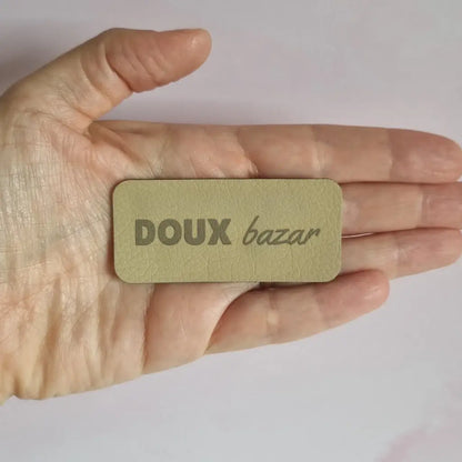 Étiquette à coudre en simili cuir gravée Doux bazar, tenue au creux de la main