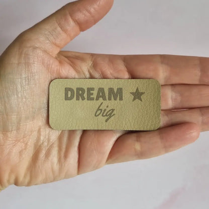 Étiquette simili cuir gravée Dream big avec petite étoile, vue de face dans la main