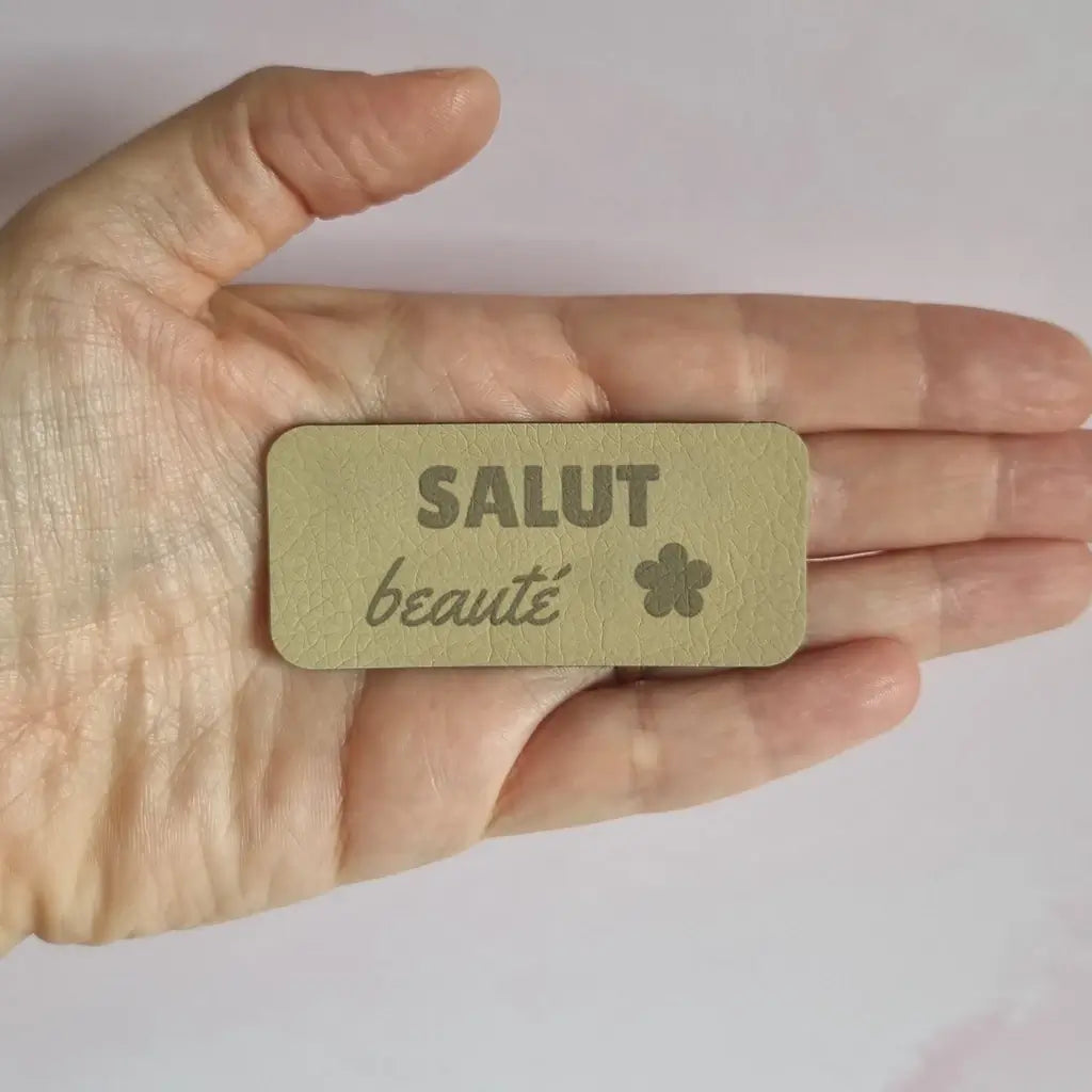 Étiquette simili cuir gravée Salut beauté avec petite fleur, tenue à la main