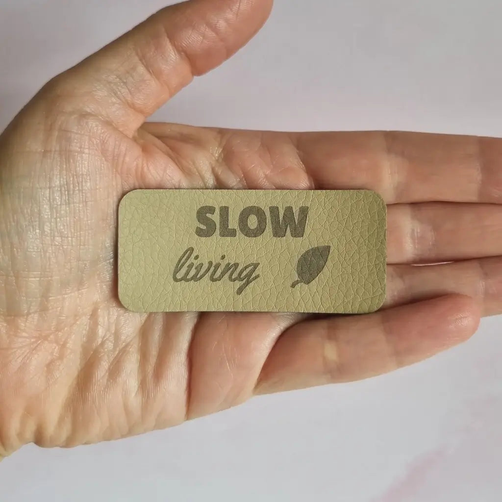 Étiquette à coudre gravée Slow living avec feuille, gros plan sur le simili cuir grainé