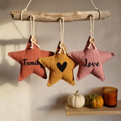 Trois étoiles décoratives en tissu rose, ocre et vieux rose suspendues à une branche, inscriptions Family, cœur et Love