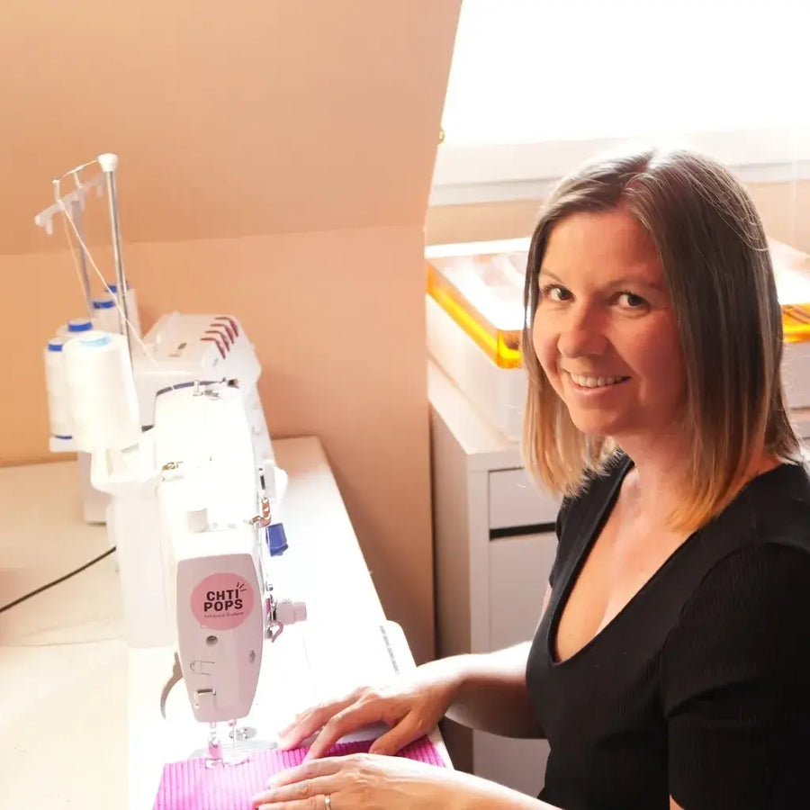 Fanny, dans son atelier Chtipops Créations, souriant devant sa machine à coudre.