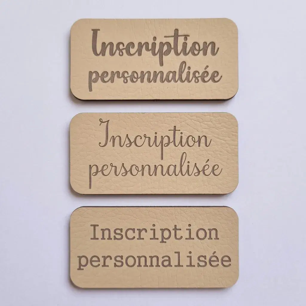 Comparaison de trois polices de gravure sur étiquettes en simili cuir beige, vue de dessus sur fond clair