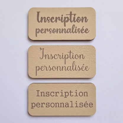 Comparaison de trois polices de gravure sur étiquettes en simili cuir beige, vue de dessus sur fond clair