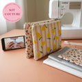 Deux pochettes plates zippées à motifs citrons et léopard devant une machine à coudre, avec tissus et zips