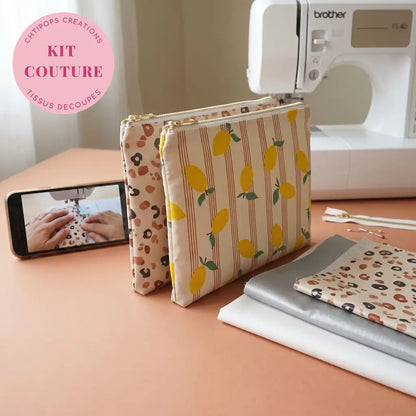 Deux pochettes plates zippées à motifs citrons et léopard devant une machine à coudre, avec tissus et zips