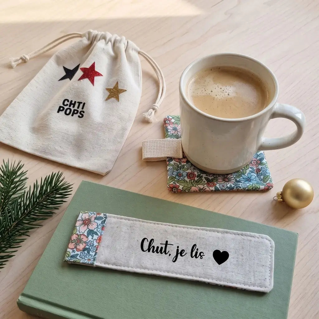 Marque-page en toile écrue et tissu fleuri « Chut, je lis » avec cœur, posé sur un livre vert dans un décor de Noël