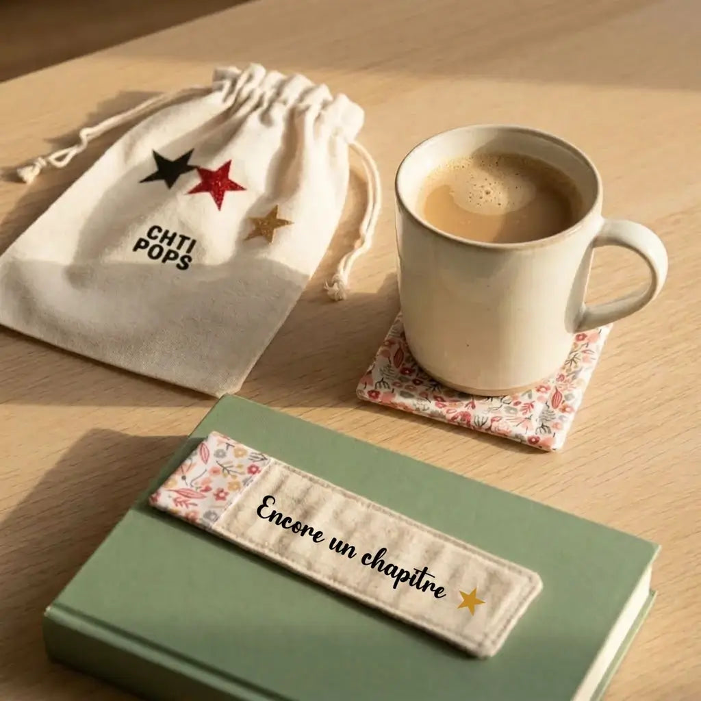 Marque-page « Encore un chapitre » avec étoile dorée et bout fleuri rose, posé sur un livre vert près d’une tasse de café