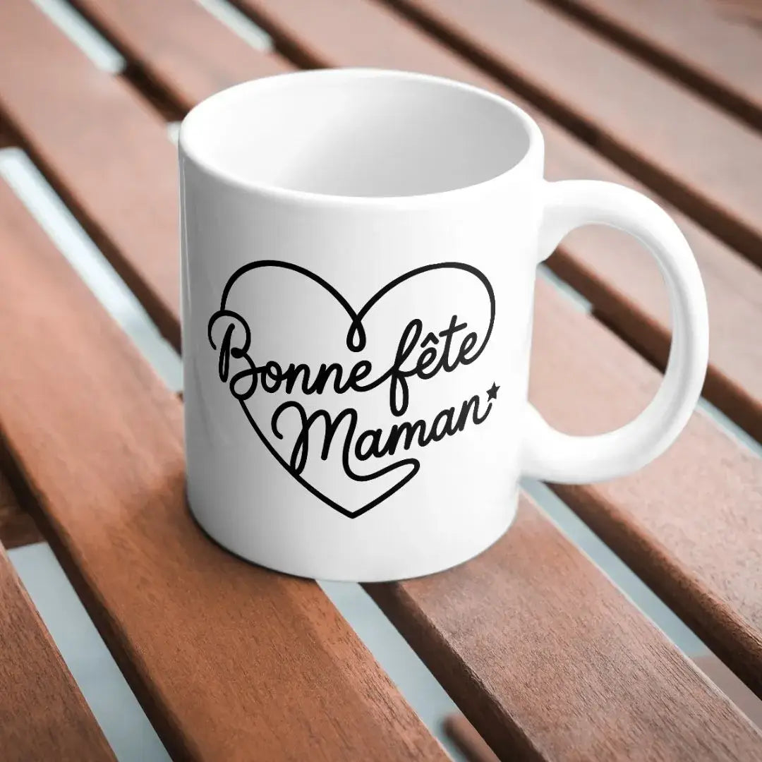 mug blanc avec texte bonne fête maman en forme de cœur imprimé en noir sur table bois
