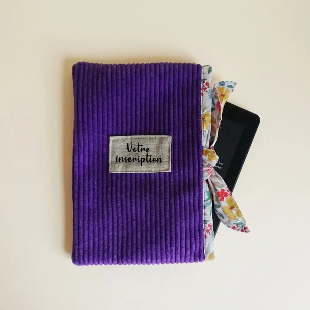 Pochette liseuse violette en velours côtelé, lien fleuri noué en haut et étiquette à personnaliser