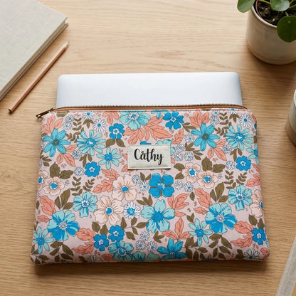 Housse ordinateur à fleurs bleues sur fond rose pâle, prénom Cathy, vue du dessus avec ordinateur portable glissé