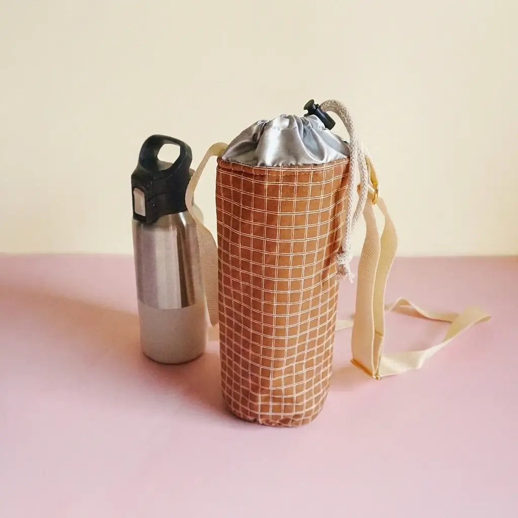 Porte-gourde marron à fins carreaux, intérieur argenté et cordon de serrage, avec gourde à côté
