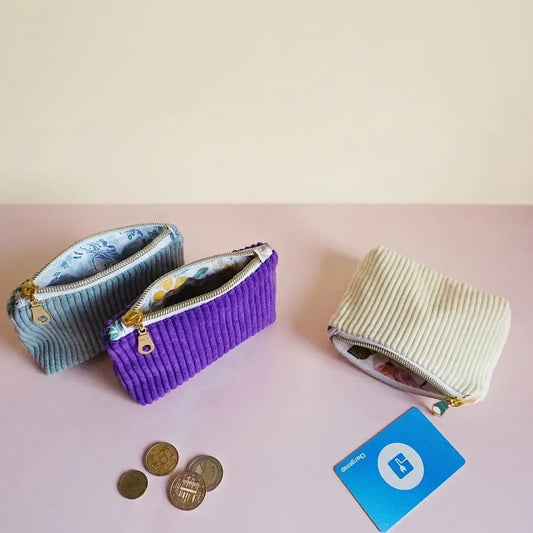 Trois porte-monnaie en velours côtelé bleu, violet et écru présentés ouverts côte à côte